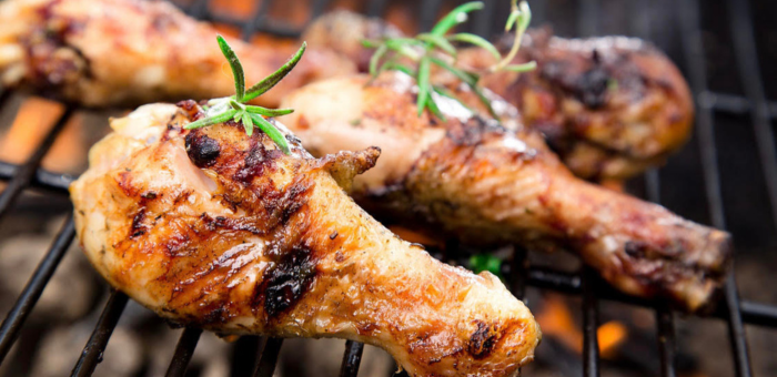 Grilled chicken drumsticks with golden-brown char marks topped with fresh rosemary sprigs on a hot barbecue grill.
