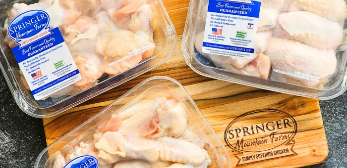 Three packs of Springer Mountain Farms raw chicken wings on a wooden cutting board with product labels and American Humane Certified™ seal visible.