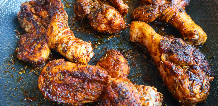 Seasoned chicken drumsticks seared in a skillet with crispy golden-brown skin and spices.