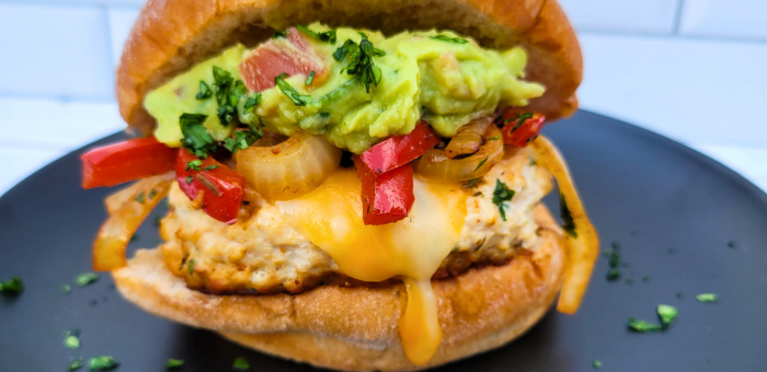 Grilled Springer Mountain Farms chicken burger topped with melted cheddar, sautéed onions and red peppers, and fresh guacamole on a toasted bun.