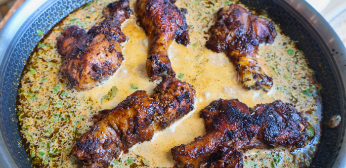 Chicken drumsticks simmering in a creamy braising sauce with herbs in a skillet.
