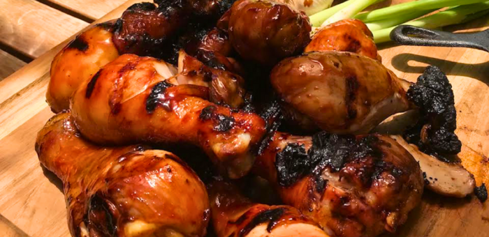Mahogany-glazed chicken drumsticks served over a colorful summer salad of cherry tomatoes and cucumbers on a white square plate.