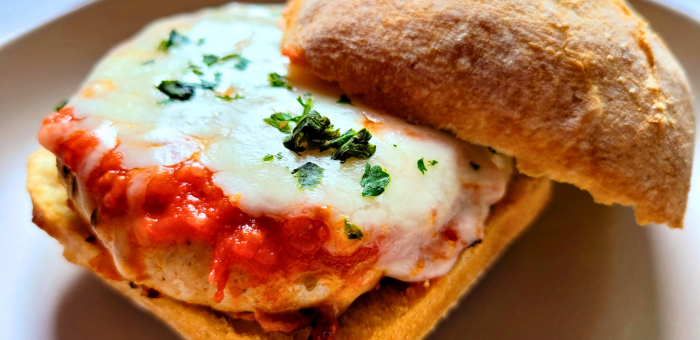 Italian-inspired chicken burger with pizza sauce and melted mozzarella cheese, garnished with basil on a toasted ciabatta roll.