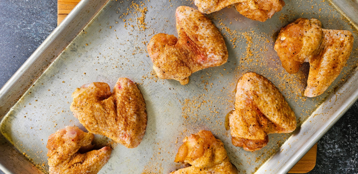Chicken wings coated in dry rub seasoning on a metal baking sheet, ready to be grilled for a smoky flavor.