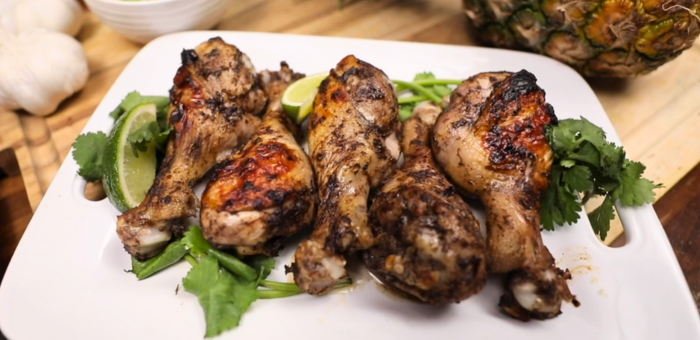 Jerk-seasoned grilled chicken drumsticks served with fresh cilantro, lime wedges, and jalapeño slices on a white plate.