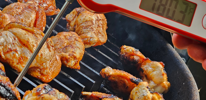 Cooked chicken wings on the grill with a meat thermometer inserted showing internal temperature over 180°F.