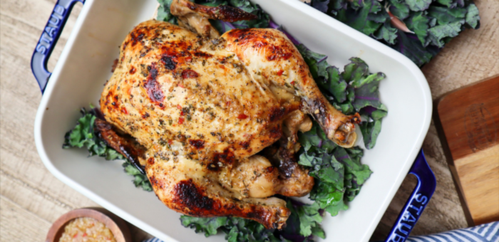 Oven-roasted Springer Mountain Farms whole chicken served on a bed of kale in a white baking dish, golden and crispy.