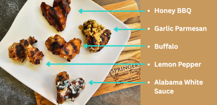 Plate of grilled chicken wings with five different sauces labeled: Honey BBQ, Garlic Parmesan, Buffalo, Lemon Pepper, and Alabama White Sauce, placed on a Springer Mountain Farms cutting board.