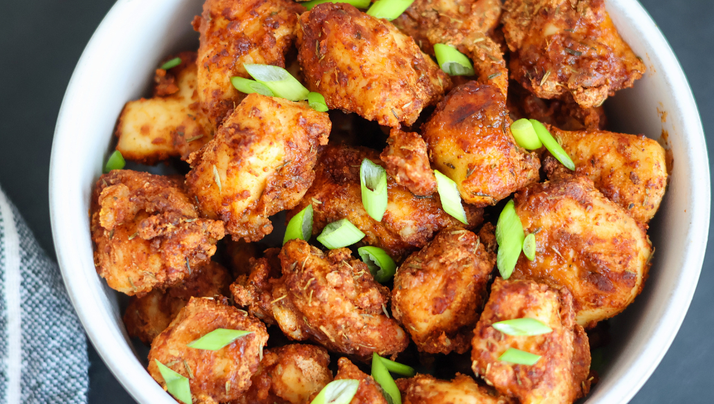 Crispy air fryer chicken bites seasoned with spices and topped with fresh green onions in a white bowl – healthy, high-protein appetizer or dinner idea.
