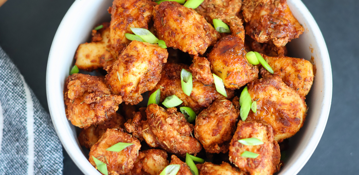 Crispy air fryer chicken bites seasoned with spices and topped with fresh green onions in a white bowl – healthy, high-protein appetizer or dinner idea.