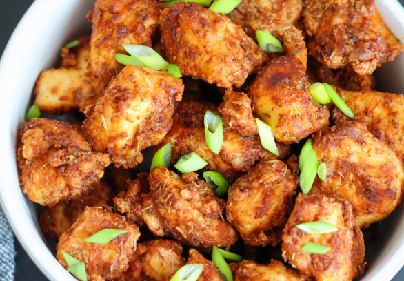 Crispy air fryer chicken bites seasoned with spices and topped with fresh green onions in a white bowl – healthy, high-protein appetizer or dinner idea.