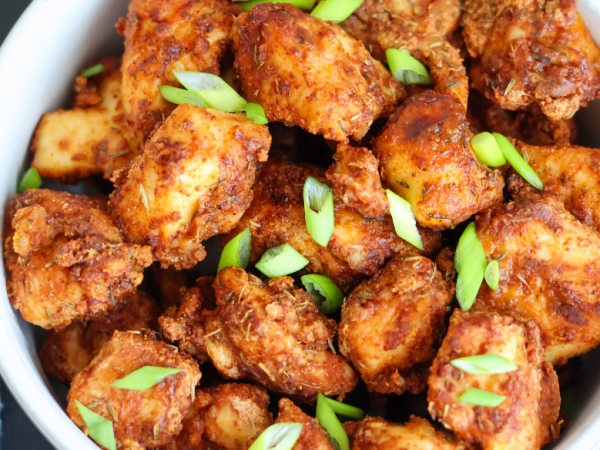 Crispy air fryer chicken bites seasoned with spices and topped with fresh green onions in a white bowl – healthy, high-protein appetizer or dinner idea.