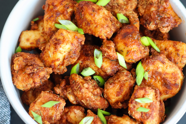 Crispy air fryer chicken bites seasoned with spices and topped with fresh green onions in a white bowl – healthy, high-protein appetizer or dinner idea.