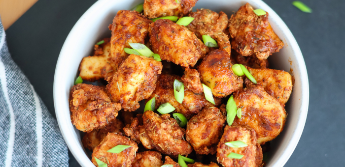 Close-up of crispy golden-brown air fryer chicken bites garnished with fresh green onions in a white bowl.
