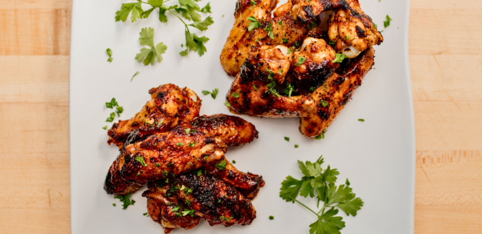 Apricot chipotle glazed chicken wings arranged on a white square plate, garnished with chopped herbs and fresh parsley, served on a light wooden surface.