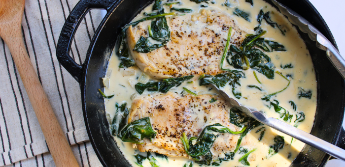 Braised chicken breasts in a creamy garlic sauce with fresh spinach in a cast iron pan.