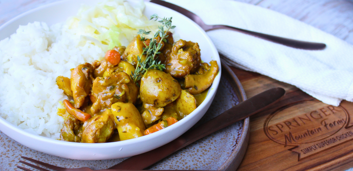 Bowl of Springer Mountain Farms chicken curry with potatoes, carrots, and rice, served with fresh thyme garnish.
