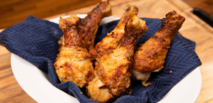 Golden, crispy buttermilk air-fried chicken drumsticks served in a white bowl lined with a dark blue cloth.
