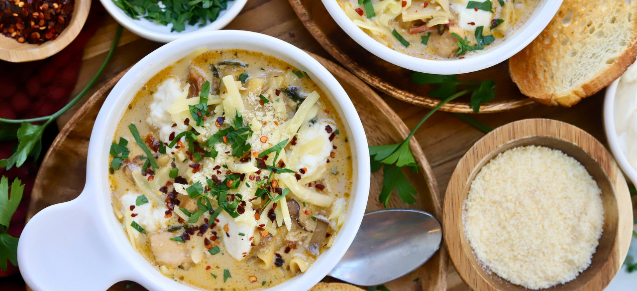 Bowl of cheesy white lasagna soup with Springer Mountain Farms chicken, topped with melted cheese, fresh parsley, and red pepper flakes, served with Parmesan and toasted bread.
