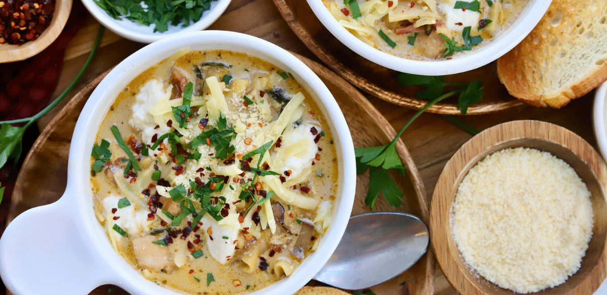 Bowl of cheesy white lasagna soup with Springer Mountain Farms chicken, topped with melted cheese, fresh parsley, and red pepper flakes, served with Parmesan and toasted bread.