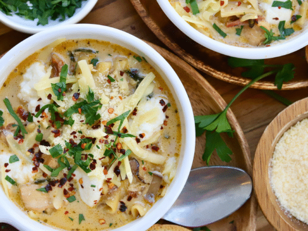 Bowl of cheesy white lasagna soup with Springer Mountain Farms chicken, topped with melted cheese, fresh parsley, and red pepper flakes, served with Parmesan and toasted bread.