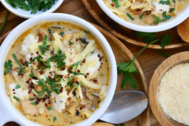 Bowl of cheesy white lasagna soup with Springer Mountain Farms chicken, topped with melted cheese, fresh parsley, and red pepper flakes, served with Parmesan and toasted bread.