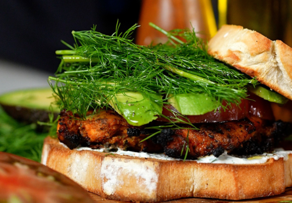 Grilled chicken bacon ranch sandwich stacked with juicy chicken breast, crispy bacon, avocado, fresh dill, heirloom tomato, and creamy ranch dressing on toasted white bread.