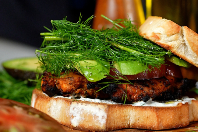 Grilled chicken bacon ranch sandwich stacked with juicy chicken breast, crispy bacon, avocado, fresh dill, heirloom tomato, and creamy ranch dressing on toasted white bread.