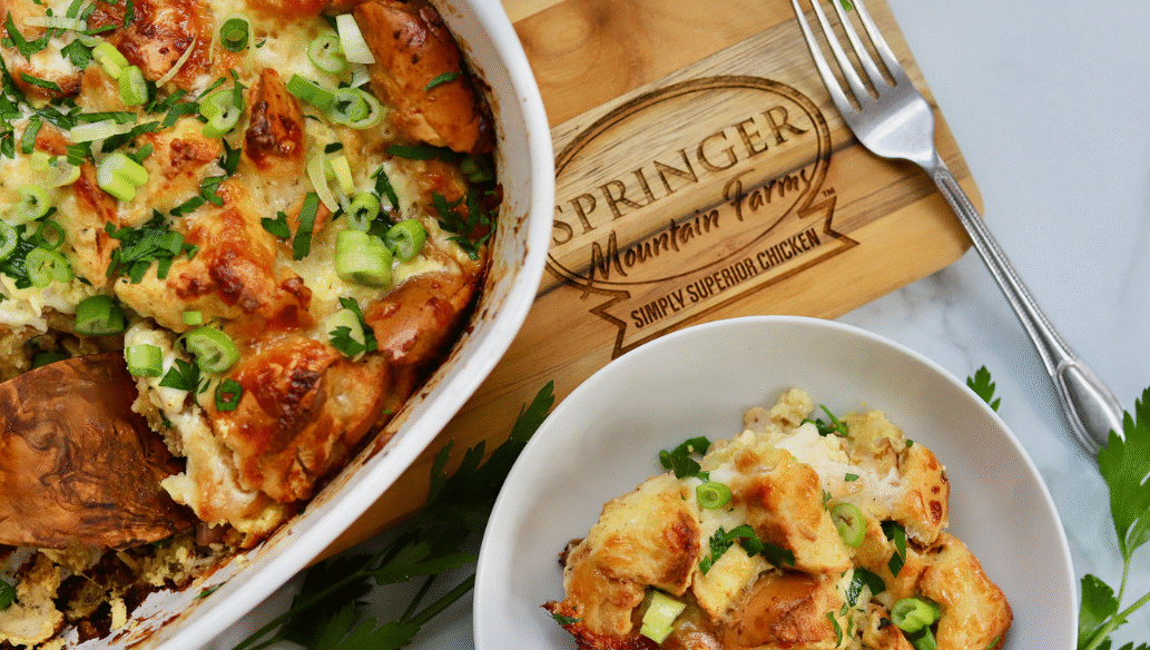 Golden baked chicken cordon bleu casserole topped with toasty bagel pieces, melted cheese, and fresh green onions, served in a dish with a side portion.