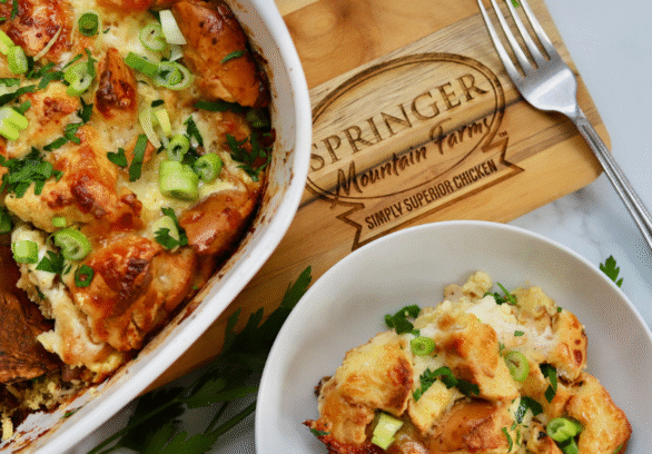 Golden baked chicken cordon bleu casserole topped with toasty bagel pieces, melted cheese, and fresh green onions, served in a dish with a side portion.