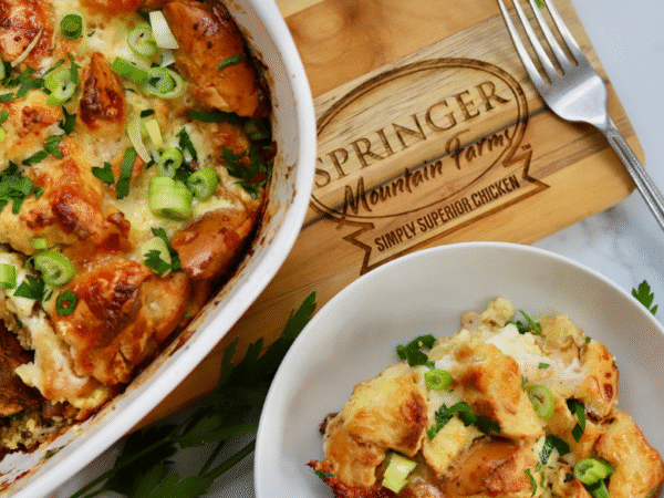 Golden baked chicken cordon bleu casserole topped with toasty bagel pieces, melted cheese, and fresh green onions, served in a dish with a side portion.