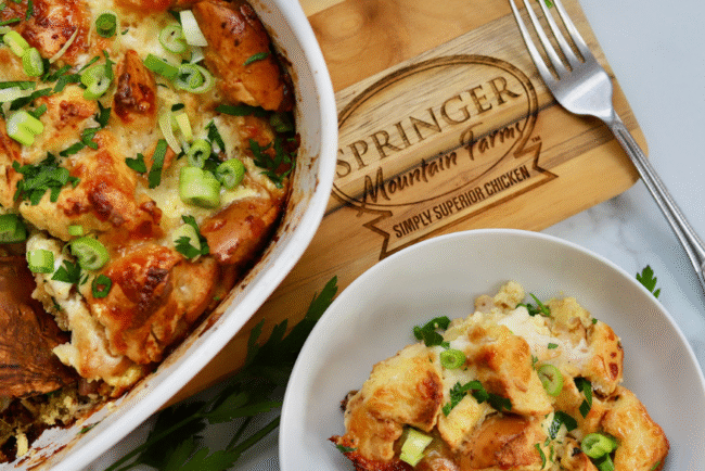 Golden baked chicken cordon bleu casserole topped with toasty bagel pieces, melted cheese, and fresh green onions, served in a dish with a side portion.