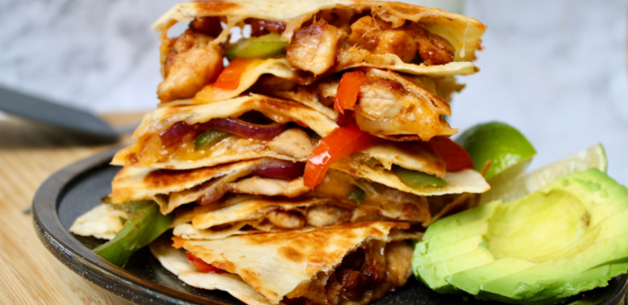 Stacked chicken fajita quesadillas filled with peppers, onions, and melted cheese, served with avocado slices and lime.