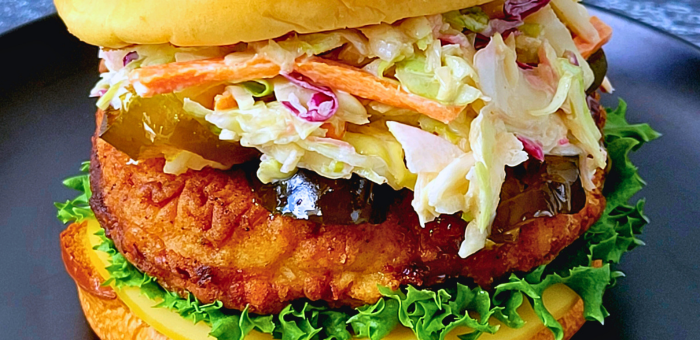 Crispy fried chicken sandwich stacked with fresh lettuce, cheddar cheese, tangy pickles, and creamy coleslaw on a toasted bun.