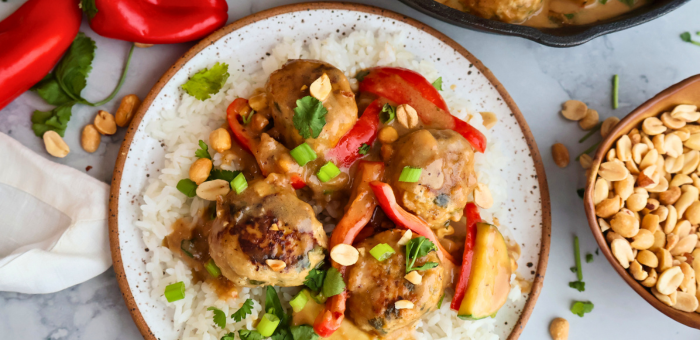 Ground chicken meatballs served over rice with creamy peanut sauce, red peppers, peanuts, and fresh herbs.