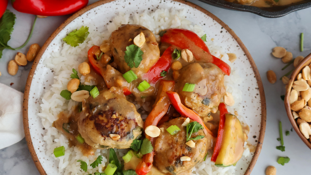Ground chicken meatballs in creamy peanut sauce served over white rice with red bell peppers, green onions, and peanuts.