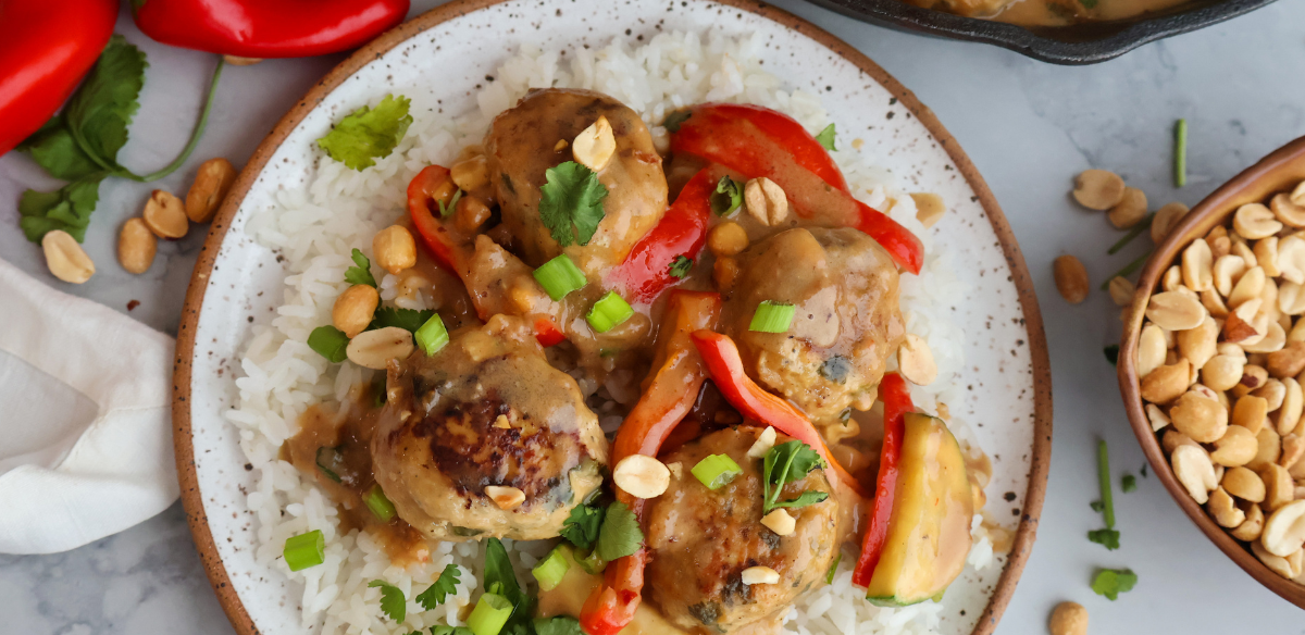 Ground chicken meatballs in creamy peanut sauce served over white rice with red bell peppers, green onions, and peanuts.