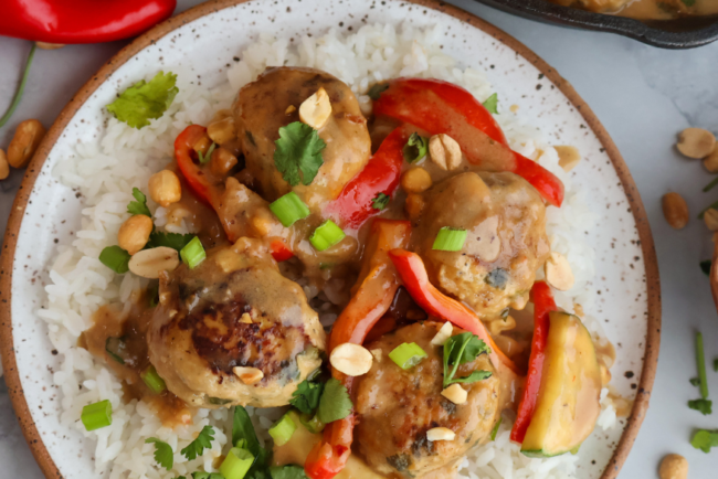 Ground chicken meatballs in creamy peanut sauce served over white rice with red bell peppers, green onions, and peanuts.