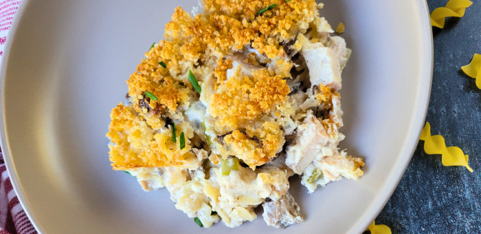 Creamy baked chicken noodle casserole with golden breadcrumb topping served on a light gray plate.