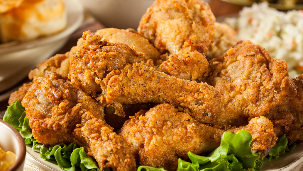 Classic Southern fried chicken drumsticks piled high on a platter with fresh lettuce, served alongside coleslaw, biscuits, and macaroni and cheese.