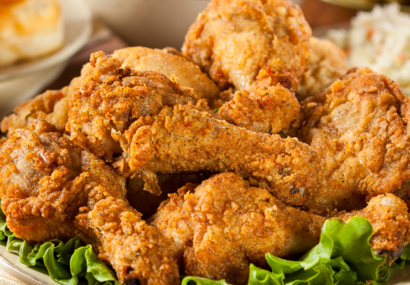 Classic Southern fried chicken drumsticks piled high on a platter with fresh lettuce, served alongside coleslaw, biscuits, and macaroni and cheese.