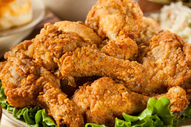 Classic Southern fried chicken drumsticks piled high on a platter with fresh lettuce, served alongside coleslaw, biscuits, and macaroni and cheese.