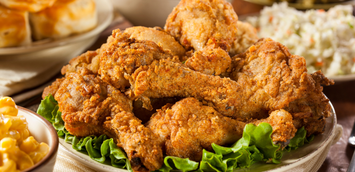 Classic Southern fried chicken drumsticks piled high on a platter with fresh lettuce, served alongside coleslaw, biscuits, and macaroni and cheese.