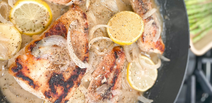Juicy chicken breasts cooked in creamy lemon sauce with onion slices and lemon rounds in a skillet.