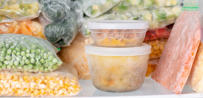 Organized freezer stocked with labeled containers of homemade meals and bags of frozen vegetables for meal prep.