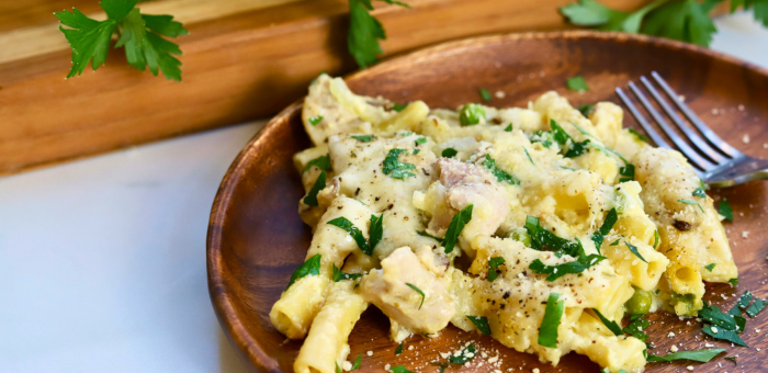 Cheesy baked chicken stroganoff pasta topped with parsley on a wooden plate.