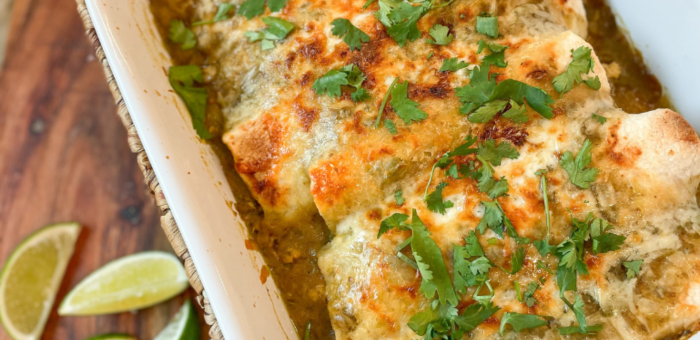 Baked green chicken enchiladas topped with melted cheese and cilantro in a casserole dish — quick make-ahead enchilada recipe with Springer Mountain Farms chicken.