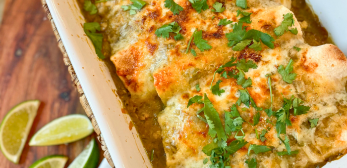 Cheesy green chile chicken enchiladas baked in a casserole dish with fresh cilantro and lime – simple Mexican-inspired dinner idea