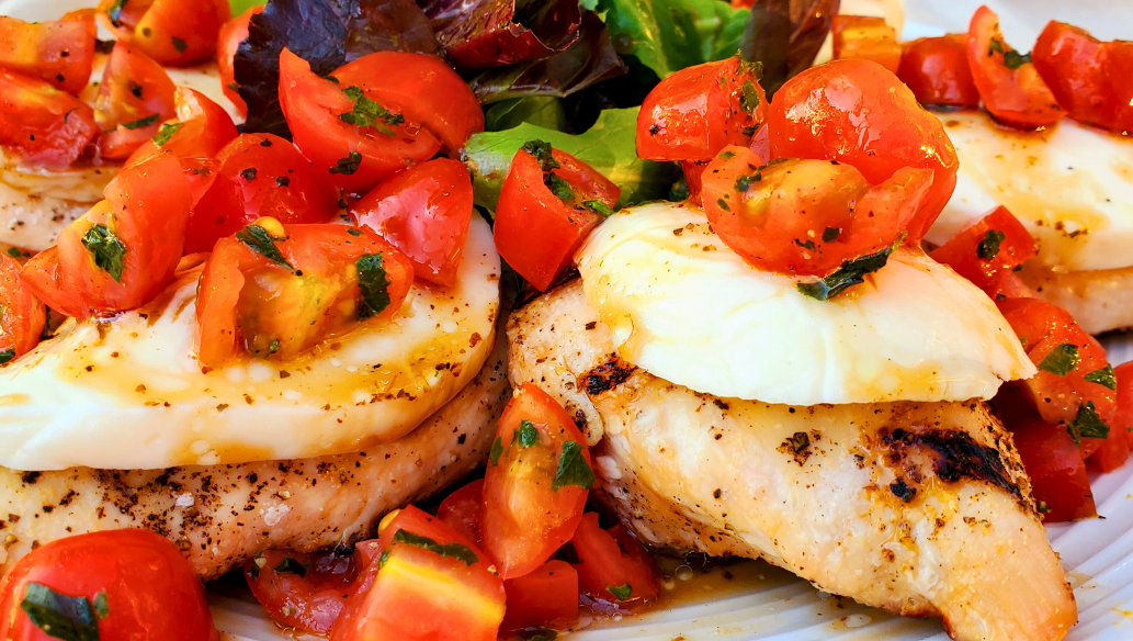 Grilled Springer Mountain Farms 4 oz boneless skinless chicken breasts topped with fresh mozzarella, cherry tomatoes, basil, and balsamic glaze for a healthy Caprese chicken recipe perfect for summer grilling.