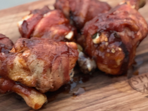 Grilled jalapeño popper stuffed chicken drumsticks wrapped in crispy bacon, glazed with barbecue sauce, served on a Springer Mountain Farms wooden board.